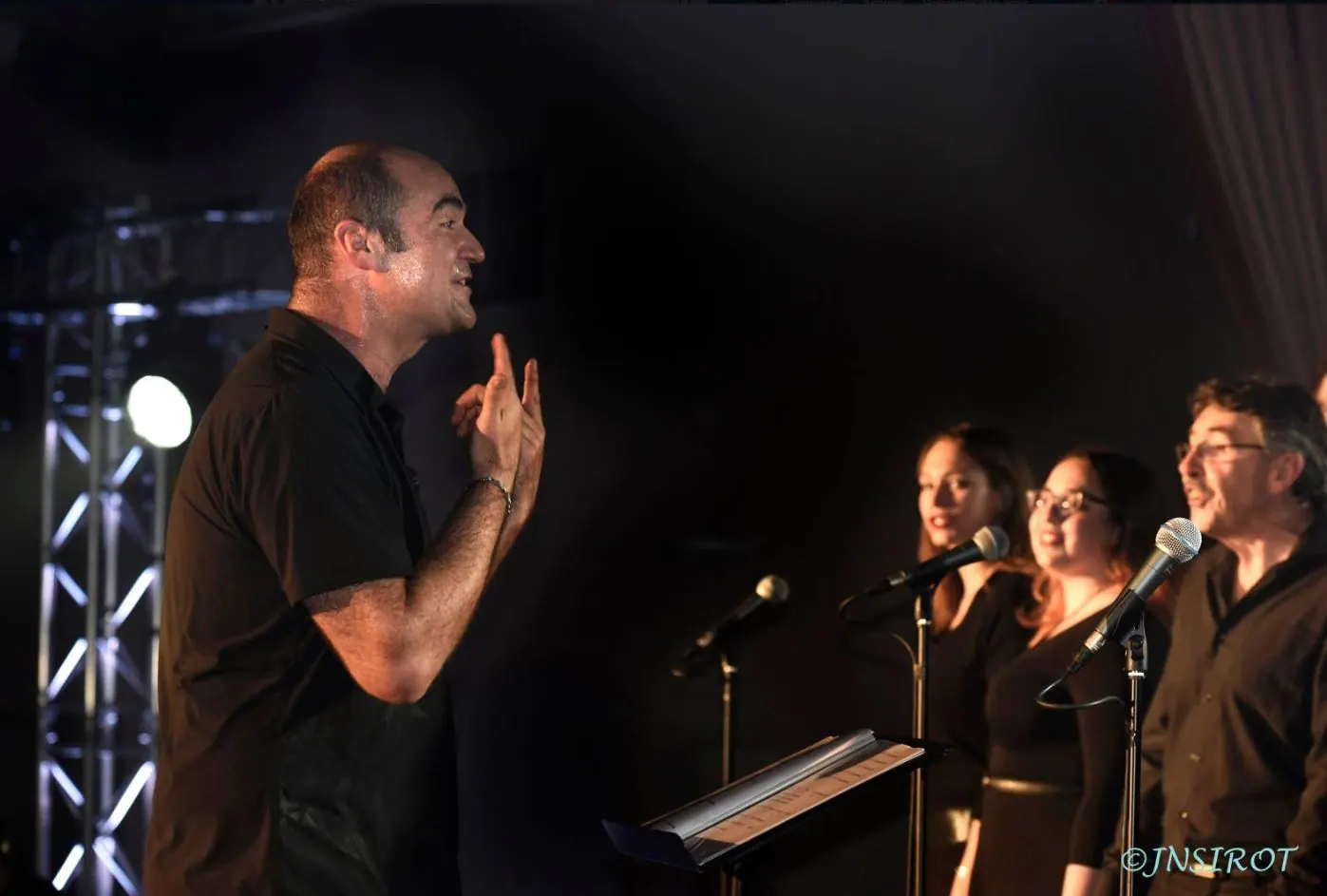 Le chef de chœur face à trois chanteurs derrière leurs micros